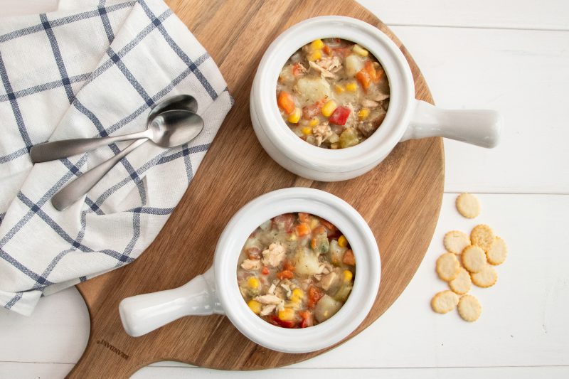 2 bowls of Hearty Pacific Chowder on a wooden circle board