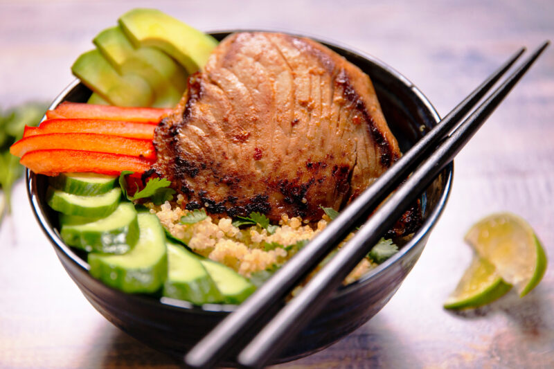 A quinoa bowl topped with a yellowfin tuna steak, cucumbers, red pepper, avovado, cilantro and lime juice.